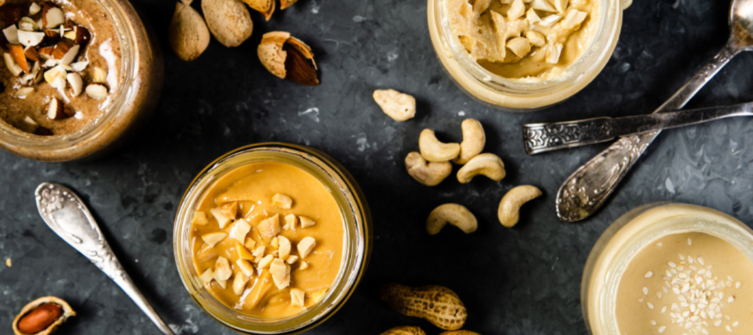 nut butters on a grey slate background with nuts scattered around them