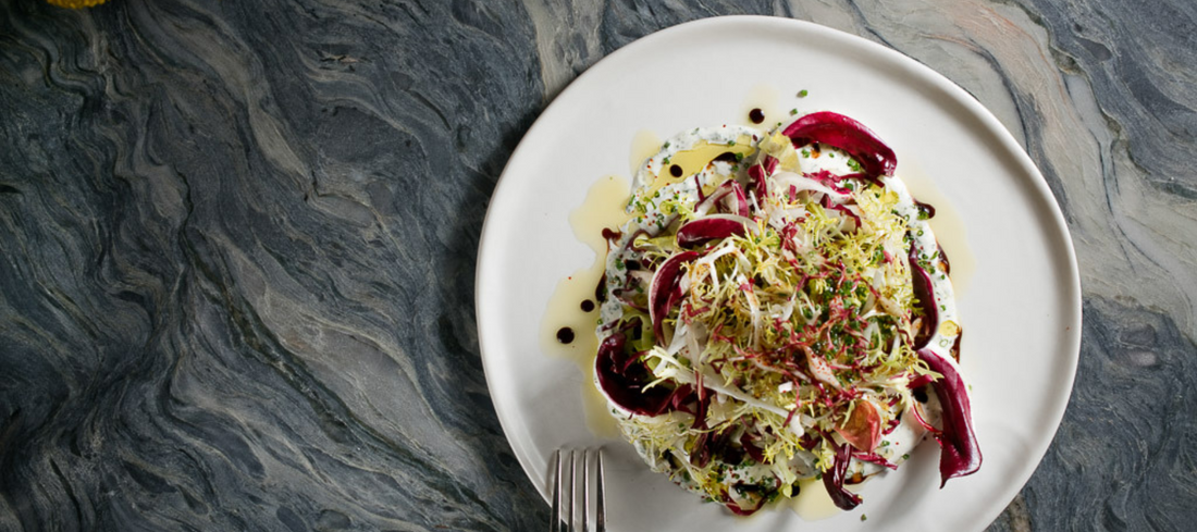 Haand ceramic plate with a colorful salad on a dark marble counter