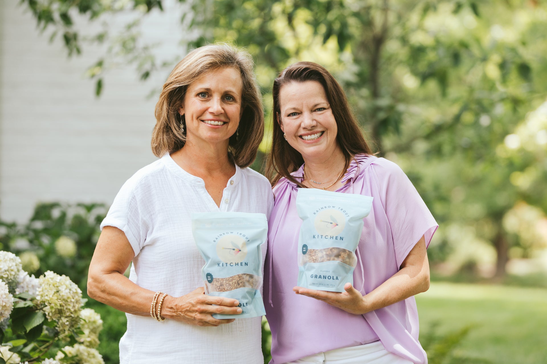 Jakie Bowles and Ashley Wallace of Rainbow Trout Kitchen granola, each holding a bag of 1 lb granola