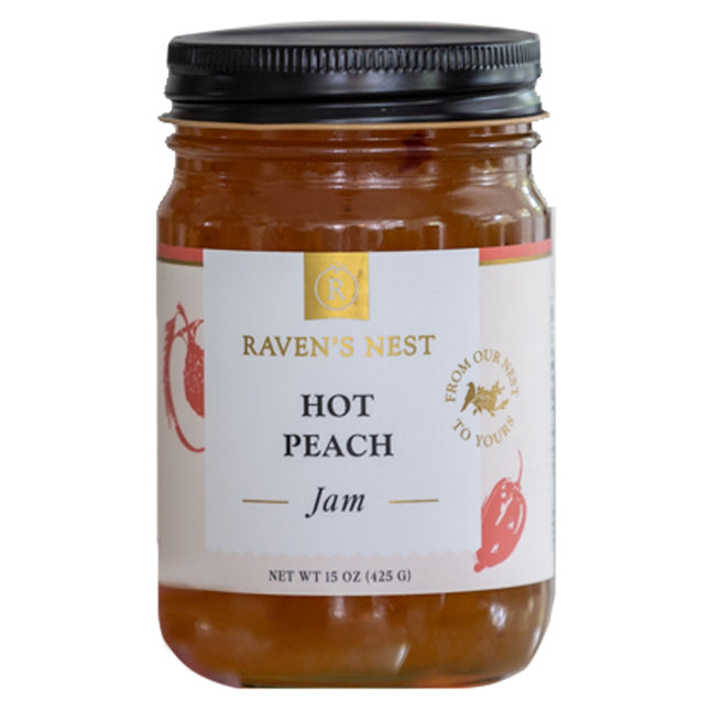 A jar of "Raven's Nest Hot Peach Jam" with a black lid and a white label featuring the brand logo